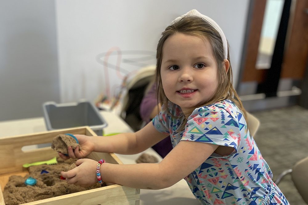 Young girl searches for treasures in a sandbox at Little Explorers program.